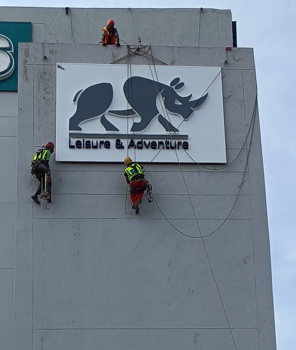 Rope-access specialists installing Leisure & Adventure exterior building signage at Parkview Shopping Centre in Pretoria East.